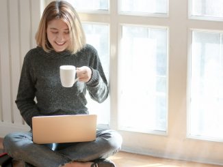 Kvinde i gråt drikker kaffe imen hun er på computeren