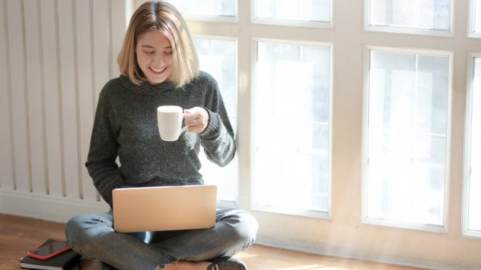 Kvinde i gråt drikker kaffe imen hun er på computeren